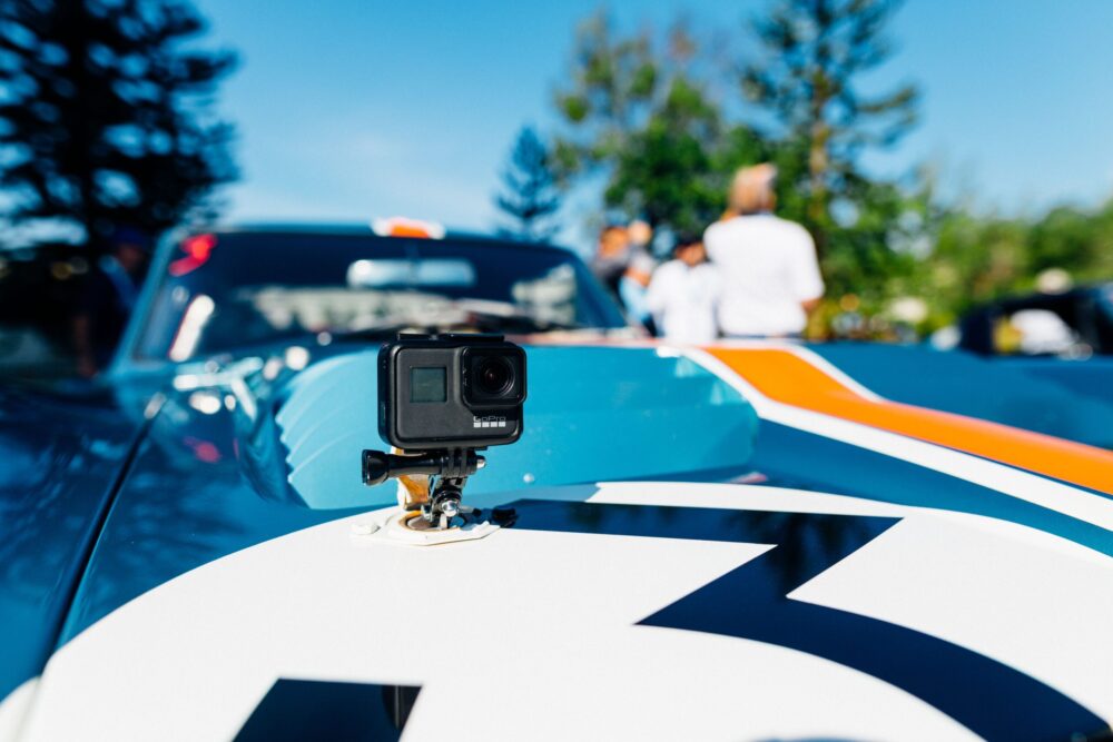 Een zwarte actioncamera is bevestigd op de motorkap van een blauwe raceauto met witte en oranje details.