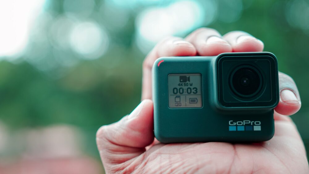 Een hand houdt een zwarte GoPro-actioncamera vast met een groothoeklens en een klein display aan de voorkant.
