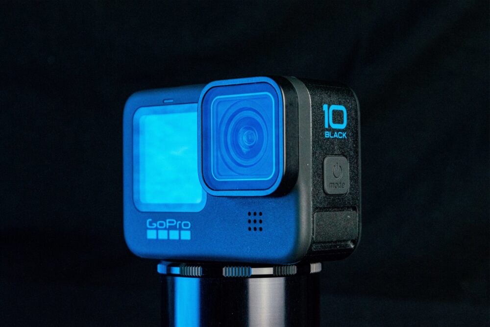 Een blauwe GoPro HERO10 Black actioncamera staat op een standaard tegen een donkere achtergrond.